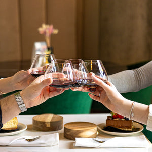 Gruppo che brinda con bicchieri in cristallo Aequilibrium di Audacem, riempiti di vino rosso, con sottobicchieri in legno, durante una cena